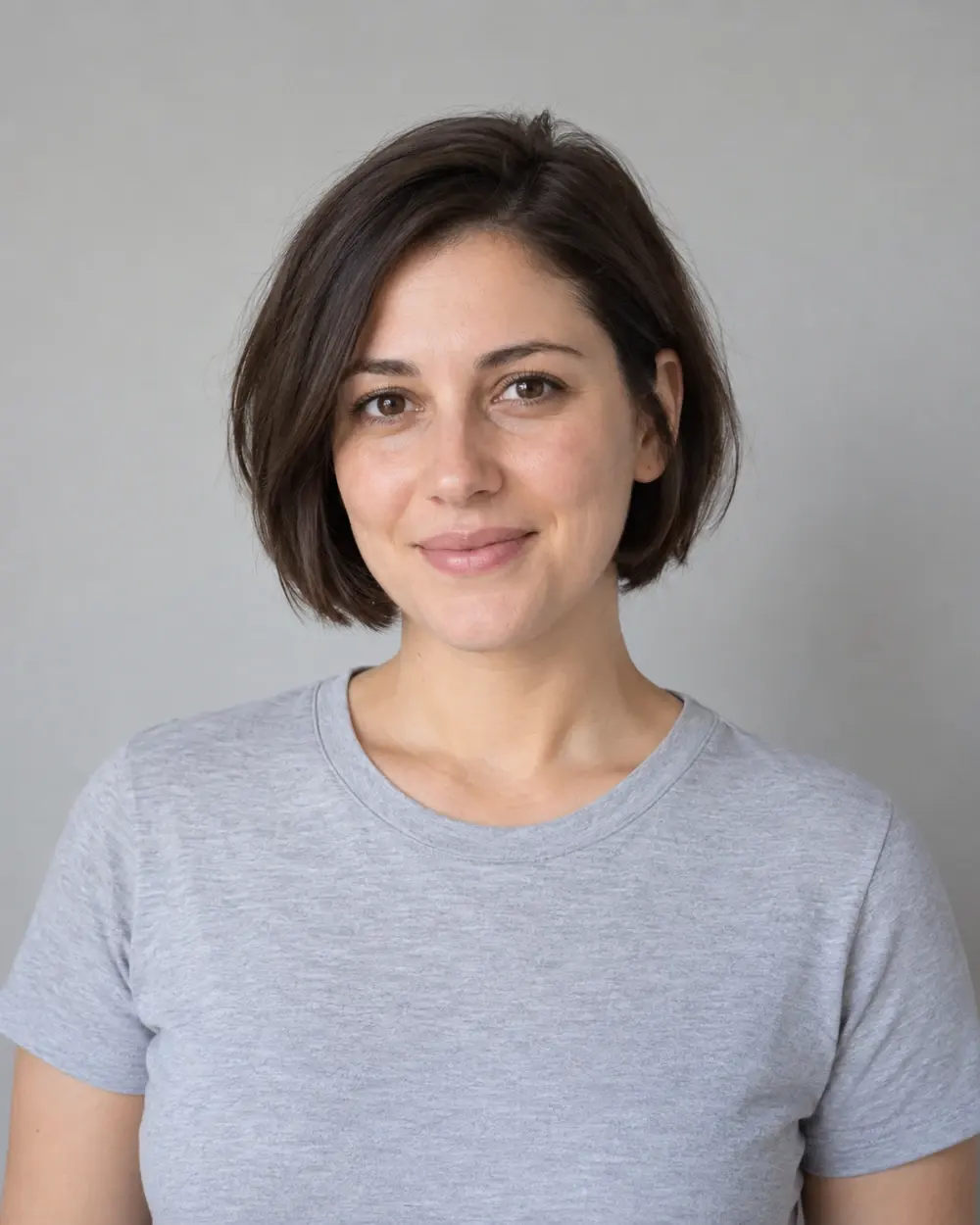 AI-generated fictional adult woman with a modern bob and gray T-shirt against a plain wall, used as the original reference